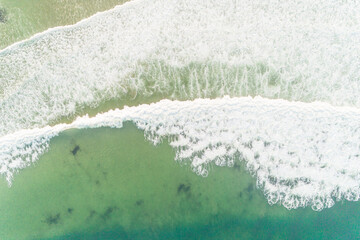aerial drone view of the waves arriving at the shore of a beach. Foam and transparent turquoise...