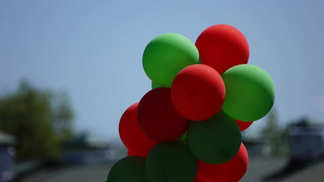 Lot of red and green balloons against background of blue sky in summer city park.