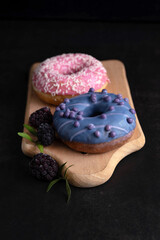 On a dark background on a wooden board there are two donuts with glaze.