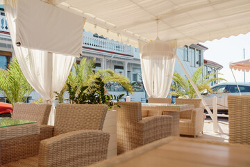 Wicker furniture tables in the open air are waiting for visitors. The interior of the restaurant in...