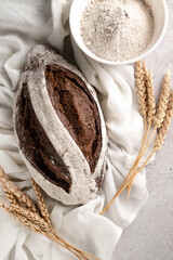 Black bread, a plate with rye flour, a textile napkin, ears of wheat on a gray table.