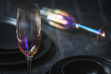 Pink shimmering champagne glass and black stoneware on a rustic black table, one glass lying in the...