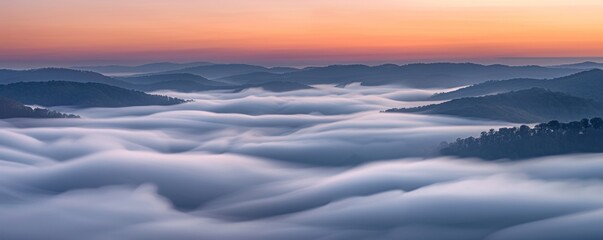 Fototapeta na wymiar Waves of fog roll over hills at dawn