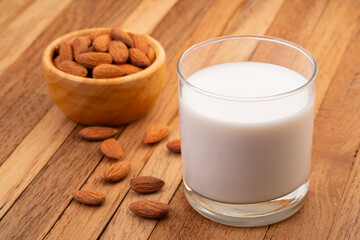Almond milk in the glass with almond on wooden plate.