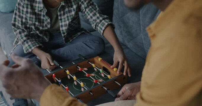 Dad and child African American people playing foosball on sofa at home enjoying leisure activity bonding. Family and entertainment concept.