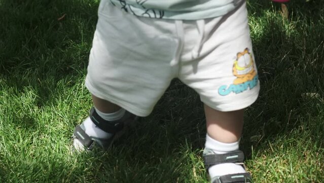Close-up of the feet of a little boy in shorts and sandals walking on the grass on a sunny day.