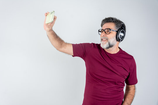 Photo of handsome man in casual t-shirt and bristle on face smiling on camera with headphones while taking selfie isolated over white background