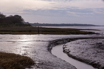 Winding Stream heading to the sea in muddy uk river Stour at Wrabness beach as the sun begins to...