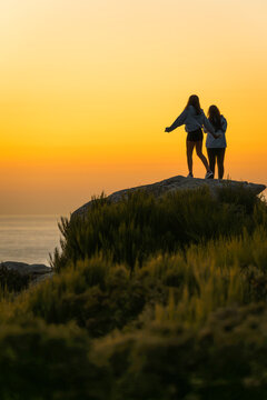 Two unrecognizable teenage girls enjoying the sunset on the seashore during vacation