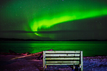 Bench by the water with a stunning aurora in the background