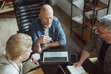Team of individuals is gathered around a table, collaborating on a laptop. They are engaged in a discussion or project, displaying teamwork and cooperation.