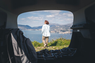 A young woman traveling by car admires the view of the sea and mountains, summer vacation auto travel