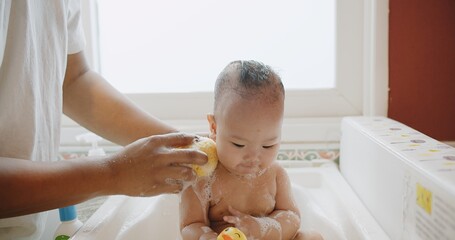 happy little cute Asian baby joy bathing in bathtub and play water having fun smiling at bathroom...