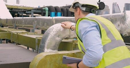 Engineer inspecting insulated pipelines at an industrial site with a digital tablet.