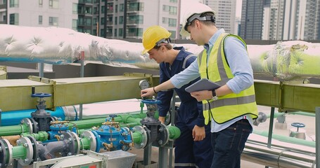 Two engineers with hard hats are checking the gauge on a pipeline valve in an urban industrial
