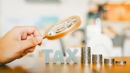 Hand holding magnifying glass looking at tax letter and money coin, stack of money rising up,...