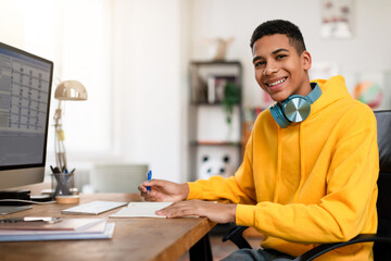 Smiling teen guy with headphones studying at desk