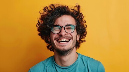 Candid portrait of a handsome curly-haired young man in a turquoise t-shirt and glasses on a yellow background laughing. copy space for text.