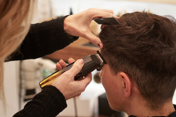 An hairdresser cuts a woman's hair with an electric razor in an hair salon - obrazy, fototapety, plakaty