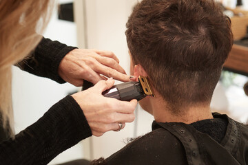 An hairdresser cuts a woman's nape's hair behind the ear with an electric razor in an hair salon - obrazy, fototapety, plakaty