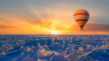 Hot air balloon flying over snowy ice hummocks with transparent blue piles of ice - Baikal Lake,...