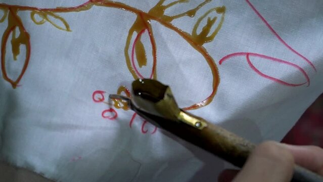 Close up footage of participants learning traditional batik making using hot wax in a pan and canting drawn on a piece of white cloth. Beginner's process of learning to paint traditional Javanese bat