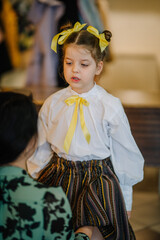 Valmiera, Latvia, April 1. 2024 - A little girl in traditional Latvian clothing looks to the side, with yellow ribbons in her hair and a bow on her blouse.