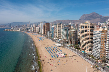 Aerial drone photo of the town of Benidorm in Spain in the summer time showing high rise apartments and building along side the Levante Beach on a sunny day with people on the beach