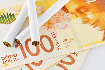 Cigarettes are on 100 shekel bills. Concept of big expenses, big price or taxes. - obrazy, fototapety, plakaty