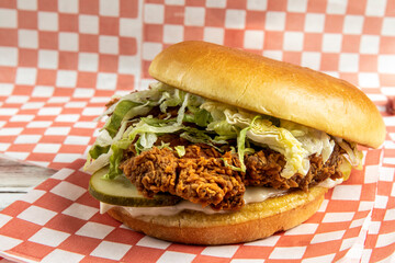a deep fried chicken breast sandwich or burger with lettuce, pickles and mayo on a red checked paper