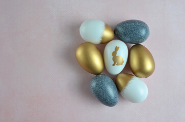 Easter eggs in navy blue, white and gold with the Easter bunny. Pink background. Easter.