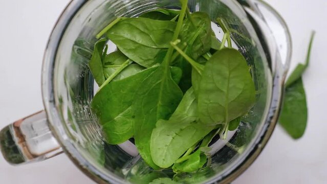 Cooking spinach smoothie in blender. Pouring green vegetable leaves in blender. Slow motion. Healthy drink concept. Top view