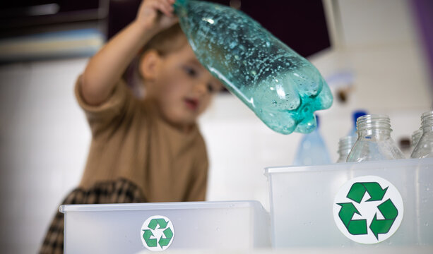 A child in the kitchen puts a plastic bottle in a drawer with a recycling sign. Close-up. In the kitchen, a cute little girl collects plastic bottles while helping her parents sort garbage.