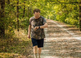 Senior man walking fast  on shady trail in spring and checking his vital signs on his smart watch