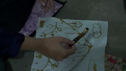 Close up footage of participants learning traditional batik making using hot wax in a pan and canting drawn on a piece of white cloth. Beginner's process of learning to paint traditional Javanese bat