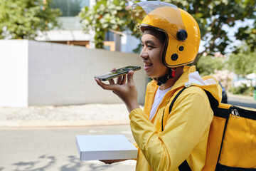 Smiling courier carrying pizza and recording voice message for customer