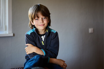 Self sufficient seven year old male child looks at camera with calm, contented look, against...