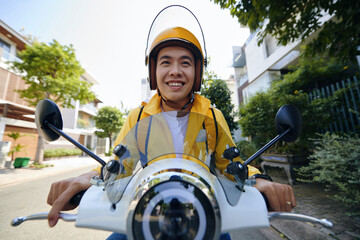 Excited Vietnamese young man riding motorbike delivering food to customers