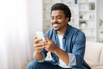 Smiling Black Man Using Smartphone in Bright Living Room