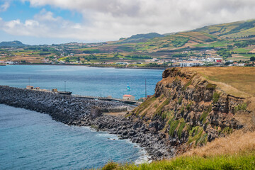 Cliff with landscape of turquoise sea and breakwater and mountains of Praia da Vitória in the background, Terceira - Azores PORTUGAL