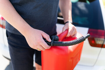 A person pouring gasoline from a red can into a car during an emergency refill.