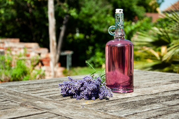 Homemade lavender syrup in a buckled bottle, placed on an old wooden table outdoors in bright...