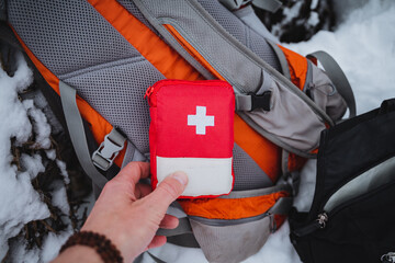 First aid kit on the background of a backpack, a man holding a red first aid kit in his hand