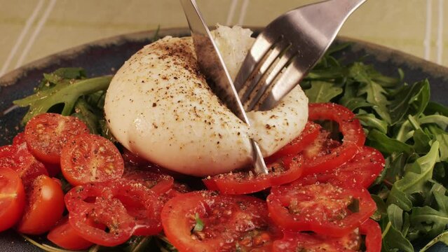 Burrata or Mozzarella cheese on fresh tomatoes and green arugula on plate close-up. From Italian cow's milk cheese made from mozzarella and cream.The outer casing is solid