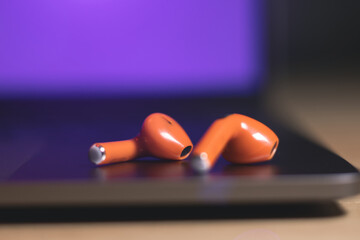 Orange Wireless Bluetooth Earphones lie on the laptop. Modern  Stereo Headphones, Sports Headset.