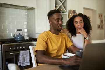 Young multiethnic couple using a laptop during breakfast at a kitchen table