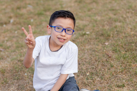 Hispanic boy playing in the field - 8 year old boy sitting on the grass in the park - Latin boy playing and having fun in nature - playing and learning - boy with white t-shirt