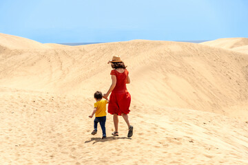 Fototapeta na wymiar Mother and son on vacation walking in the dunes of Maspalomas, Gran Canaria, Canary Islands