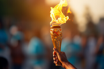 A hand of black athlete holds the cup with an torch against a blurred colorful background. Olympic torch.