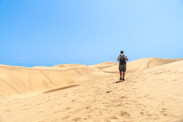 Fototapeta na wymiar A tourist walking through the dunes of Maspalomas, Gran Canaria, Canary Islands